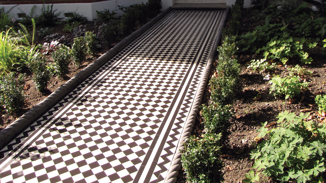 Black and White Victorian checker board path tiles. Victorian black and white tiles with zigzag border, bordered by rope-top edging and newly planted garden shrubs.