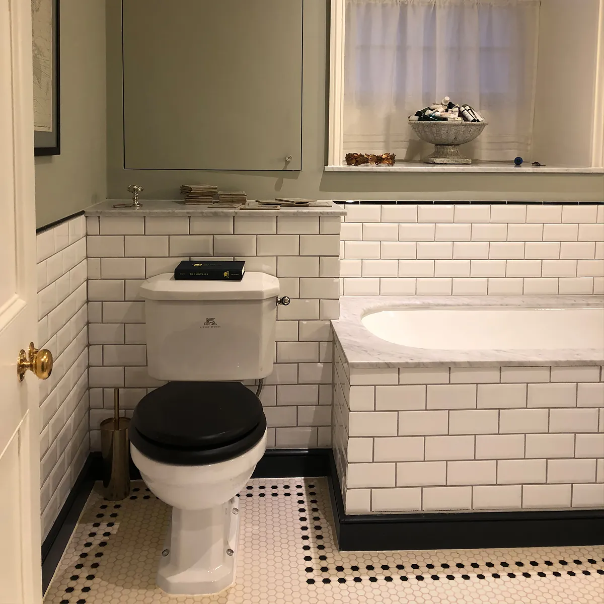 Classic white glazed metro tiles wrap around the walls and bath panel. On the floor a field of white 25mm hexagons with a simple border motif of black hexagons.