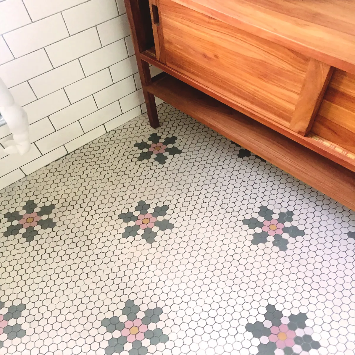 A plain field of 25mm hexagon tiles, features a repeating floral bmotif in green, pink and yellow. A wooden vanity unit sits alongside white glazed wall tiles.