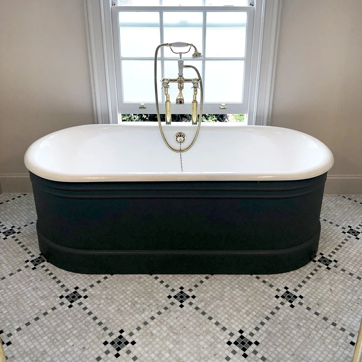 A traditional bathtub sits on a diamond set pattern of square marble mosaic in a luxury bathroom.