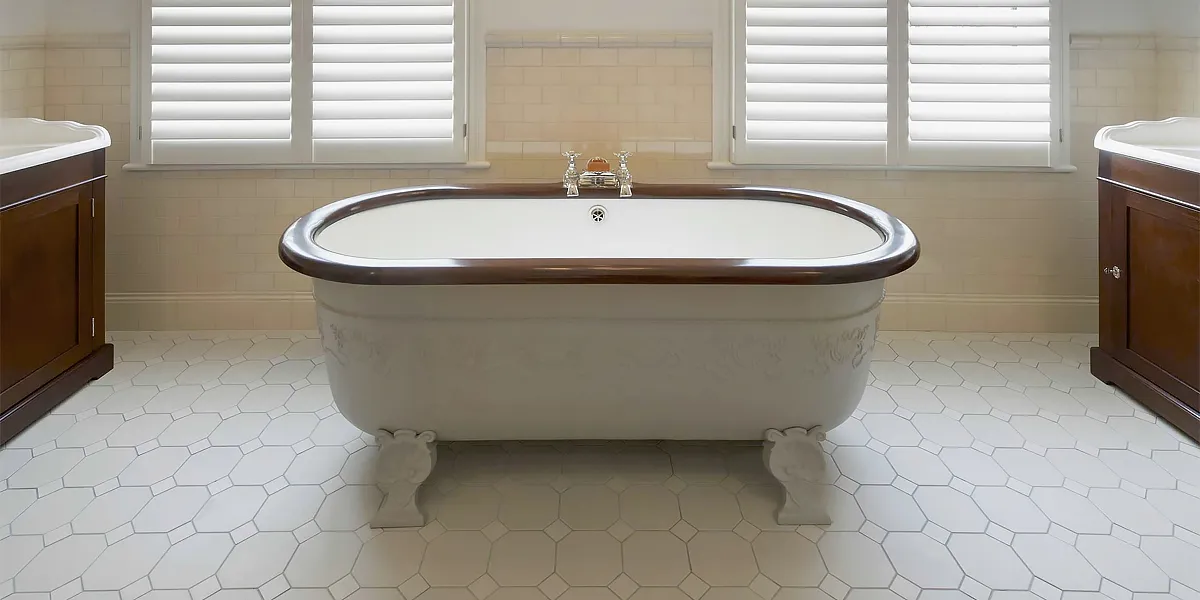 Traditional Victorian free-standing bathtub on floor of white octagon and dot tiles.