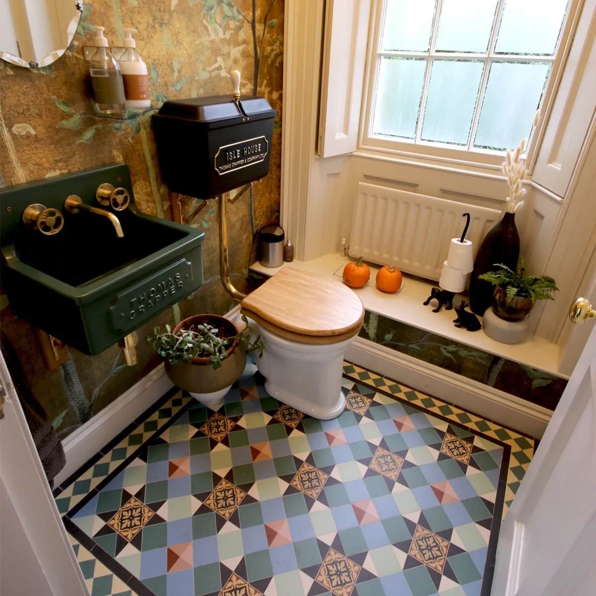 Highly decorative mosaic floor tiles in a small toilet which features vintage style fittings, and richly patterned wall paper.